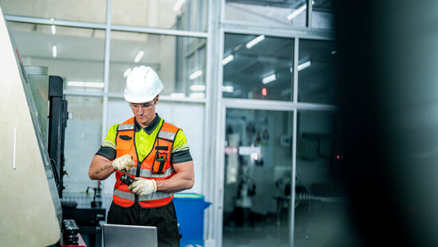 A diverse team of engineers in hard hats and safety vests operates a high-tech machine. They are programming the advanced equipment in a futuristic smart factory.