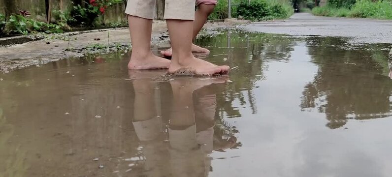 Bare feet of children splashing in a muddy puddle after rain. 
