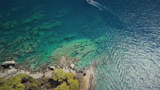 Drone view of a small boat sailing through clear turquoise water in the Gulf of Antalya, Turkey. Sunlight sparkles on the sea surface.