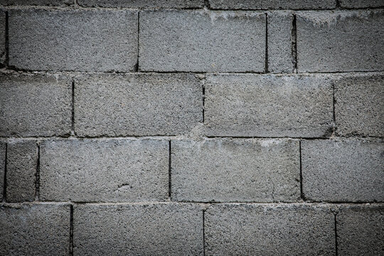 Closeup of a concrete masonry unit wall with gray, rough texture. Staggered bond and mortar joints create a repeating pattern, offering an industrial construction background made of cement blocks.