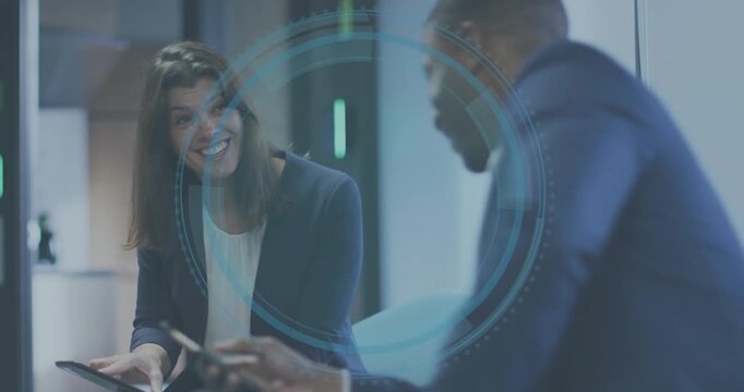 Woman pointing at tablet triggers translucent blue HUD while man nodding, reviewing business data