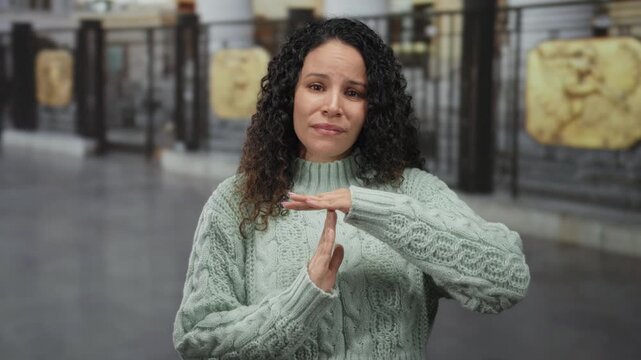 Woman gesturing timeout in urban setting with curly hair and green sweater on city street showcasing a thoughtful expression amidst outdoor urban cityscape.