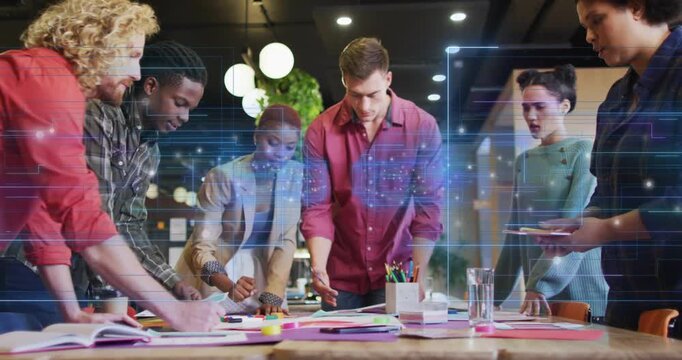 Team lead pointing while team arranging mockups on table, digital grid overlay guiding design