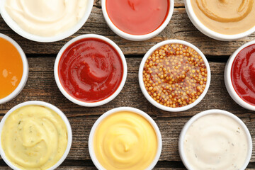 Different sauces in bowls on wooden table, flat lay