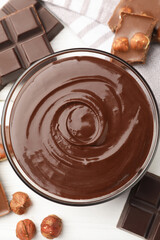 Melted chocolate and pieces with hazelnuts on white wooden table, flat lay