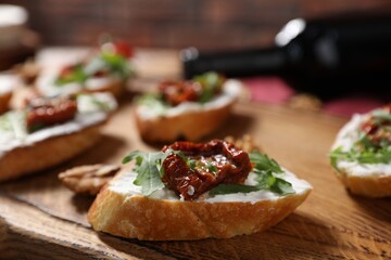 Delicious bruschettas with cream cheese, sun-dried tomatoes, arugula and bottle of wine on wooden table, closeup