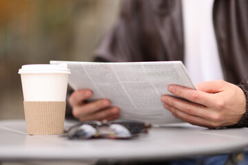 Young man reading newspaper at table in outdoor cafe, closeup