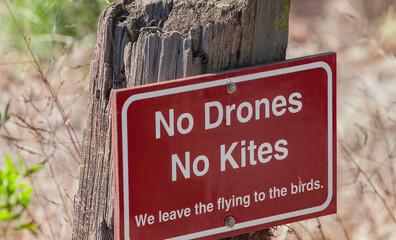 No drones or kites sign on wooden post in dry grassy area