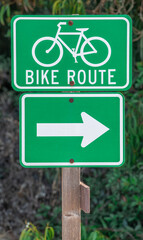 Bike route sign with directional arrow and foliage on wooden post in California
