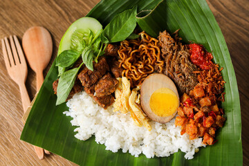 Nasi langgi is an Indonesian dish, served with rice and various side dishes like shredded beef, eggs, noodles, tempeh, potatoes, spiced grated coconut, chili, cucumber, and lemon basil.