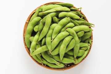 Top view of a basket with vibrant green edamame pods, displayed on a clean white background. A popular and healthy snack.