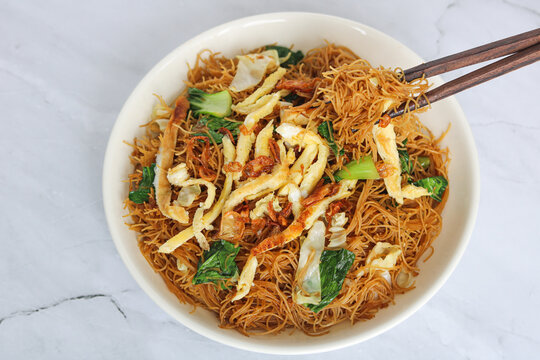 Eating fried vermicelli noodles with chopsticks. The dish is topped with shredded omelet egg, fried shallots, and green vegetables.