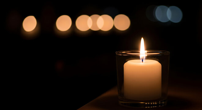A single lit candle casting a warm glow in the darkness with soft bokeh lights in the background, creating a serene and peaceful atmosphere