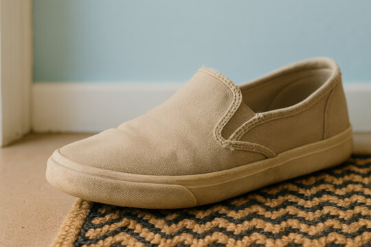 Casual beige slip on canvas shoe on zigzag patterned entryway mat with light blue wall background, minimal home footwear