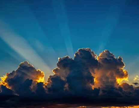 Majestic crepuscular rays of sunlight shining brightly from behind silhouetted clouds against a deep blue sky during a glorious sunset - Powered by Adobe