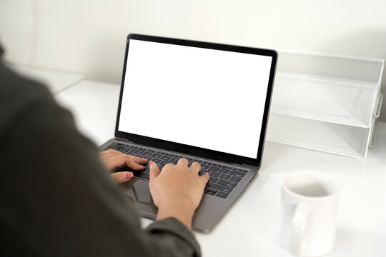 Overhead shot of hands typing on a laptop with a blank screen next to a coffee mug on a clean white desk.