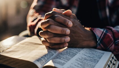 Man's hands clasped in prayer on an open Bible in warm sunlight, concept for religious devotion, spiritual reflection and faith based inspiration