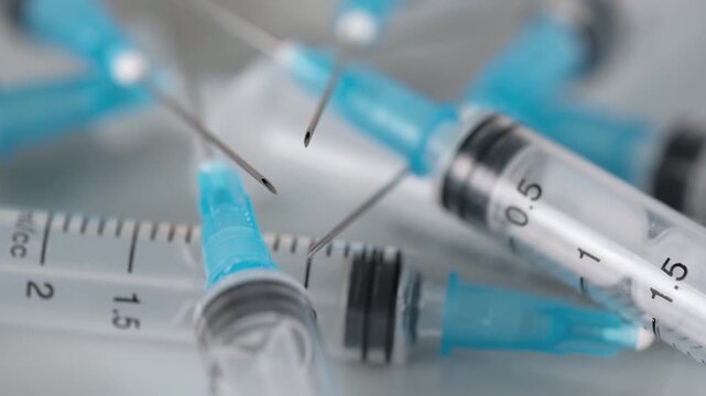 many medical plastic syringes with sharp needles rotating, representing vaccination, immunization, healthcare treatment, or drug addiction issues in clinical setting on white background. close up.