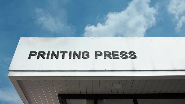 A Printing Press word sign displayed on an industrial publishing or factory building under a clear blue sky, symbolizing manufacturing, media production, publishing, and graphic industry