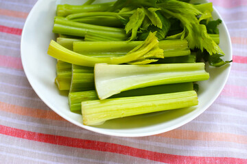 Fresh celery stalks cut into short pieces on a striped cloth.