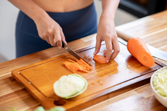 Close up sportswear woman holding knife chopping carrot on cutting board at kitchen cooking counter.