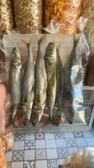 Authentic dried fish delicacy in a transparent bag, held by hand, showcasing traditional preserved seafood for sale in a vibrant market setting