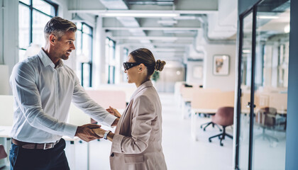 Coworker assisting blind colleague crossing modern office aisle, supportive teamwork, inclusive workplace, professional attire, bright open workspace, positive interaction