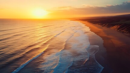 Aerial view of a beautiful sunset over the ocean with waves crashing on the sandy shore.