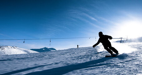 Skier carving through fresh snow on a bright sunny day with mountain slopes and ski lifts in the background © Nikola Spasenoski