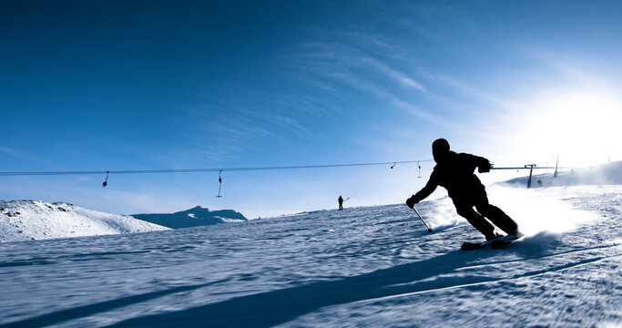 Skier carving through fresh snow on a bright sunny day with mountain slopes and ski lifts in the background
