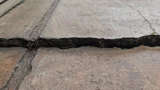 zoomed out view of cement textured concrete ground shows significant damage, with cracks and subsidence on the floor of a home or a street road caused by an earthquake. Close up view
