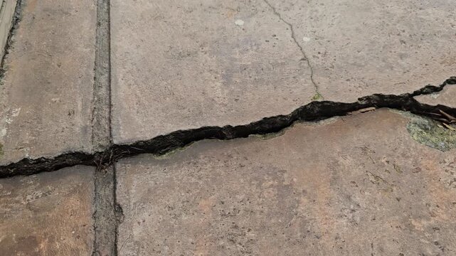 Top view of cement textured concrete ground has broken, with cracks and subsidence on the floor of a home or a street road caused by an earthquake.
