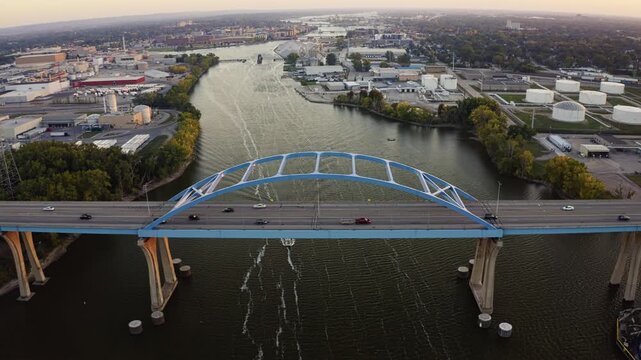 The Leo Frigo Memorial Bridge stretches across the Fox River toward downtown Green Bay, where golden sunset light reflects on the water and illuminates the industrial landscape beyond.