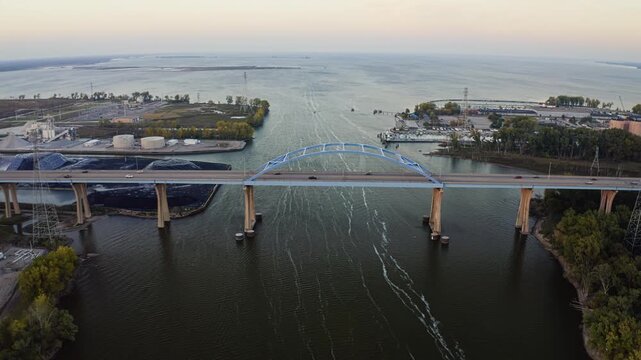 The Leo Frigo Memorial Bridge arches across the Fox River toward the vast waters of Green Bay, its pale blue steel contrasting with calm evening reflections and the city&rsquo;s industrial waterfront.