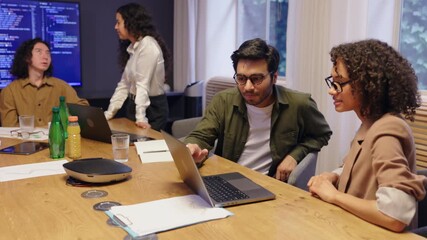 Diverse coworkers sitting around conference table in modern office working on laptop and discussing project ideas showing teamwork collaboration creativity and professional business communication - Powered by Adobe