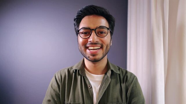 Smiling young south Asian man wearing glasses posing confidently in modern office showing positivity approachability and professionalism in a bright contemporary business environment