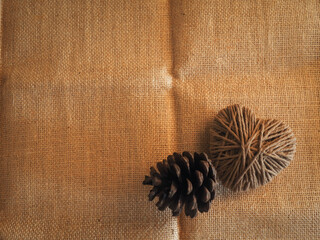 Heart-shaped yarn with pine cones on brown fabric for a minimalist copy space.