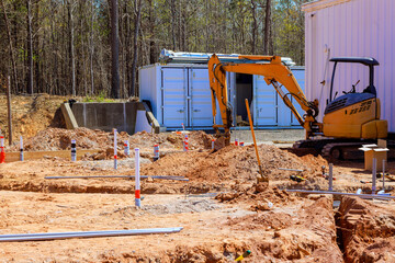 Excavator digs at construction site surrounded by trench, preparing foundation, to utility...