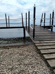 Naklejka premium Wooden pier with rope railings by the quiet water and cloudy sky. The vertical frame is the background for banners and advertisements.