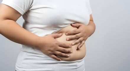 Close-up of overweight man pinching belly fat in studio, Man grabbing stomach showing body fat against gray background, Midsection of heavy-built man in white t-shirt and dark shorts, Body image and w