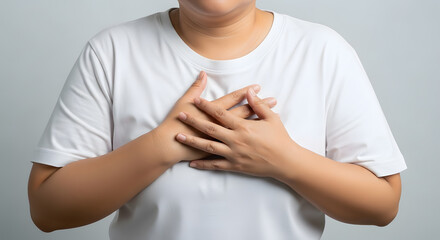Close-up of person holding hands over chest in discomfort, Mid-torso shot showing chest pain or emotional expression, Adult with light brown skin pressing hands on chest, Studio image of hands layered