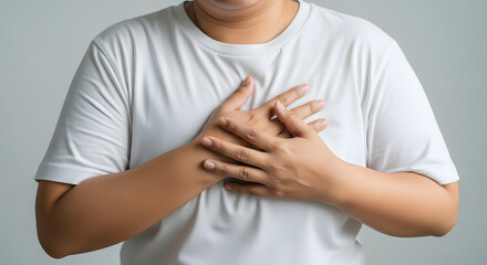 Close-up of person holding hands over chest in discomfort, Mid-torso shot showing chest pain or emotional expression, Adult with light brown skin pressing hands on chest, Studio image of hands layered
