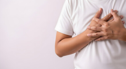 Close-up of person holding hands over chest in discomfort, Mid-torso shot showing chest pain or emotional expression, Adult with light brown skin pressing hands on chest, Studio image of hands layered