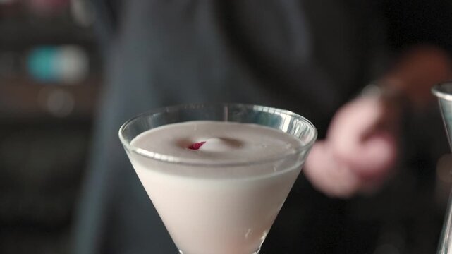 A fresh raspberry drops into a martini glass, creating ripples in the drink.