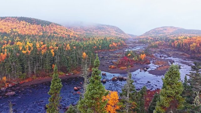 Drone panorama of colorful autumn valley with meandering river, ponds and bright orange, yellow and green forest across rolling hills.
