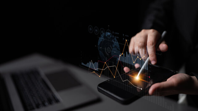Hands interact with a smartphone displaying vibrant digital charts, symbolizing modern analytics and finance trends in a dark, sleek workspace environment. Scalp
