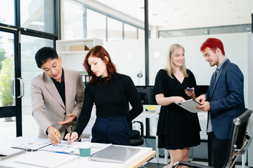 Diverse business team collaborating with laptops, tablets, and reports in a modern office, symbolizing strategy, teamwork, and corporate success.