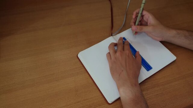 Hands and pen tracing lines in a journal notebook for calendar layout - medium static shot