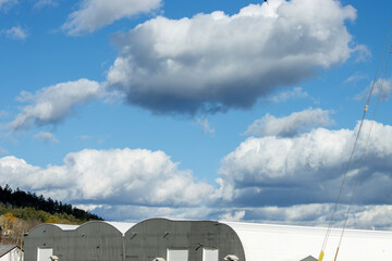 Fluffy white clouds and blue sky over a white industrial building