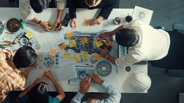 Top view of smart engineer team in casual cloth talking about turbine engine structure at table with metal gear, calculator, sticky notes. Group of technician taking a note in meeting. Alimentation.